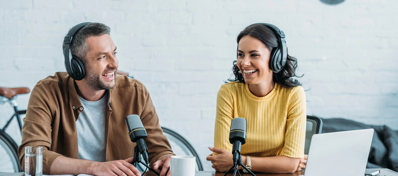 Dos presentadores de podcast con auriculares grabando un episodio frente a micrófonos en un estudio