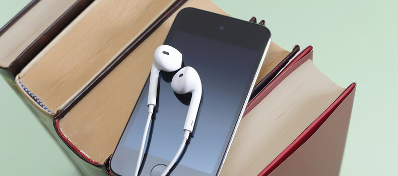 Móvil con auriculares blancos apoyado sobre una pila de libros, para escuchar audiolibros