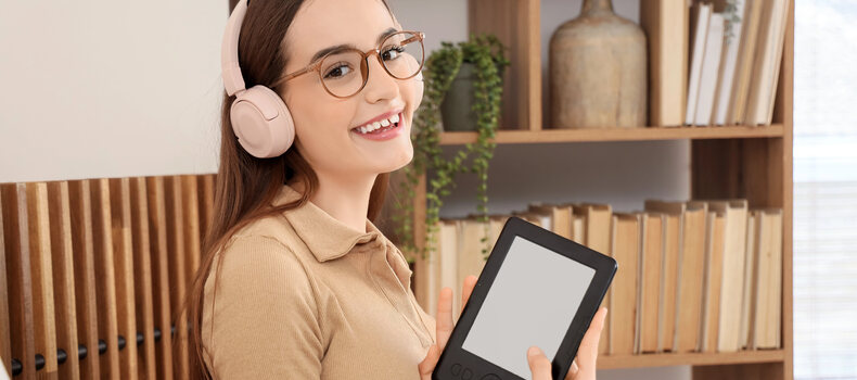 Chica con gafas y auriculares sonriendo con un lector de libros electrónicos en la mano